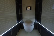 Подвесной унитаз в туалете, по стене проложена неоновая подсветка